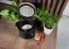 A black multi-cooker with its lid open sits on a wooden table, surrounded by green plants and a serving of yogurt with strawberries. Voir les images du produit