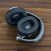 A pair of black over-ear headphones folded and resting on a wooden surface. Podgląd zdjęcia produktu
