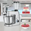 A silver kitchen appliance with multiple attachments, including a blender and a meat grinder, is shown on a countertop. A bowl of ground meat with onions and parsley is in the foreground. Produktbild-Vorschau