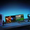 A gaming setup with a laptop and an external monitor displaying games, along with a microphone and headphones. Náhľad obrázku produktu