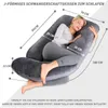 A woman is lying on a large, J-shaped pregnancy pillow, demonstrating its use for comfort and support. Produktbild-Vorschau