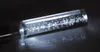A close-up shot of a glass tube with air bubbles inside, resting on a dark reflective surface. Produktbild-Vorschau