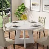 A round white dining table with four beige chairs set in a dining room with a large window overlooking a garden. Náhľad obrázku produktu