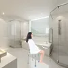 A woman sits on a shower stool in a modern, well-lit bathroom. Náhľad obrázku produktu