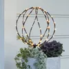 A decorative sphere with lights sits in a planter with plants. Produktbild-Vorschau