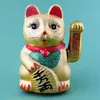 A golden Maneki-neko (lucky cat) figurine with red ears and a red scarf, sitting against a teal background. Produktbild-Vorschau