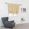 A beige tie-up Roman shade window curtain is shown hanging over a window in a room with a gray armchair and a small side table. Voir les images du produit