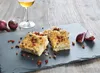 A slate platter with pieces of food and red onions, next to a glass of white wine on a wooden table. Produktbild-Vorschau