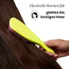 A hand is holding a bright yellow hairbrush with pink bristles, brushing through long, dark brown hair. Text overlays describe the product's features. Náhled obrázku produktu