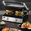 A close-up shot of a grill with two burgers being cooked, along with some side dishes. Podgląd zdjęcia produktu