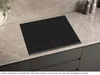A black induction cooktop is shown on a marble countertop, with dark cabinets below. Produktbild-Vorschau