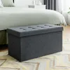 A dark gray storage ottoman is placed in front of a bed in a bedroom setting. Anteprima dell’immagine prodotto