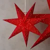 A close-up shot of red paper star lanterns hanging against a textured gray background. Produktbild-Vorschau