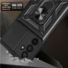 A black phone case with a camera cover and ring holder is shown on a dark, textured surface, with cracks suggesting it's being dropped. Náhľad obrázku produktu
