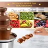 A chocolate fountain with various fruits and pastries displayed around it, and a hand dipping a skewer into the chocolate. Podgląd zdjęcia produktu