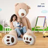 A woman and a child are sitting on the lap of a giant teddy bear in a room with a whiteboard and toys. Anteprima dell’immagine prodotto