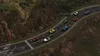 A race between several colorful cars on a winding road through a mountainous, forested area. Produktbild-Vorschau