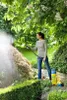 A woman is using a pressure sprayer in a garden. Produktbild-Vorschau