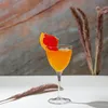 A cocktail glass with an orange drink and a grapefruit slice garnish, set against a textured background with dried grass elements. Produktbild-Vorschau