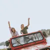 Four young people are enjoying a ride in a red convertible jeep, with two women in the back waving and smiling, and two men in the front. Anteprima dell’immagine prodotto