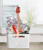 A white storage basket filled with toys, including a stuffed monkey, a stuffed animal, and a toy guitar, placed on a windowsill with plants visible outside. Voir les images du produit