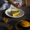 Stück Cheesecake mit grüner Pistazienglasur auf weißem Teller beim Anschneiden mit Gabel Produktbild-Vorschau