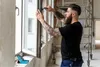 A man is installing a window in a building under construction. Voir les images du produit