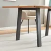 A close-up view of a table leg and part of the tabletop, with a chair visible in the background. Podgląd zdjęcia produktu