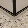 A close-up view of the corner of a shower enclosure, showing the black frame and the speckled floor. Produktbild-Vorschau