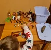 A child's hands are playing with a collection of toy animals on a wooden table. There is also a blue plastic bin and a tray with a toy rhinoceros. Anteprima dell’immagine prodotto
