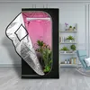 A grow tent with plants inside, set up in a room with a bookshelf and chair. Produktbild-Vorschau
