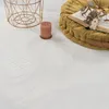 A close-up view of a fluffy white rug with a candle, a decorative basket, and a yellow floor cushion with a book on it. Produktbild-Vorschau