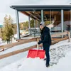 A man is shoveling snow in front of a modern building with large windows. Náhled obrázku produktu
