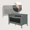 A hand is shown adjusting a part of a travel crib, with a faded image of the crib in the background. Voir les images du produit