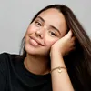 A young woman with freckles rests her head on her hand, wearing a black t-shirt and a gold bracelet with a heart-shaped charm. Voir les images du produit