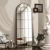 A tall, arched mirror with a black grid frame is placed in a room with a chair, candles, and a bust on a pedestal. Produktbild-Vorschau