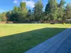 A large, well-maintained lawn with a wooden fence in the background. A riding lawn mower and a yellow object are visible on the grass. Produktbild-Vorschau