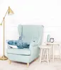 A plush shark toy is placed on a light blue armchair, next to a small side table with a vase and an alarm clock. A floor lamp is on the left. Podgląd zdjęcia produktu