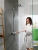 A woman in a white bathrobe is adjusting a shower head in a modern bathroom. Anteprima dell’immagine prodotto