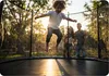 A family is enjoying a trampoline in a backyard setting during sunset. Produktbild-Vorschau