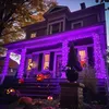 A house decorated for Halloween with purple string lights and pumpkins on the porch and lawn. Produktbild-Vorschau