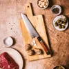 A Japanese chef's knife is placed on a wooden cutting board, surrounded by ingredients like raw beef, jerusalem artichokes, capers, peppercorns, and mushrooms. Podgląd zdjęcia produktu