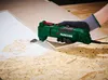 A person wearing gloves is using a green oscillating multi-tool to scrape off material from a surface. Produktbild-Vorschau