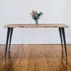A wooden table with black metal legs and a vase of flowers on top, set against a white wall and wooden floor. Náhľad obrázku produktu