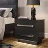 A modern black high-gloss nightstand with silver handles and integrated LED lighting, placed next to a bed.