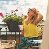 A woman is sitting on a balcony with flowers and a cup of coffee. Voir les images du produit