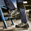 A person wearing work pants and safety shoes is stepping onto a blue metal ladder in an industrial setting. Anteprima dell’immagine prodotto