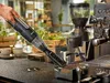 A hand is using a black handheld vacuum cleaner to clean coffee grounds from a coffee machine. Podgląd zdjęcia produktu