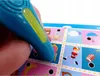 A hand holding a blue talking pen over a colorful learning game board with various images. Náhled obrázku produktu