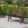 A wooden garden bench sits on a paved patio in front of a lush green hedge with pink flowers. Náhled obrázku produktu